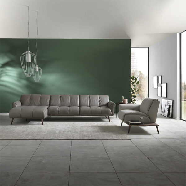Transform your modern living room with the B993 TALENTO Living Room Set, featuring a grey sectional sofa and matching armchair. Highlight the space with a green accent wall and geometric pendant lights. Large windows flood the room with natural light, while minimalistic decorations like a rug and side table complete the look.