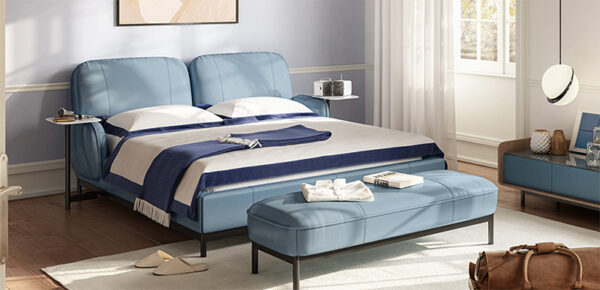 A modern bedroom with a LE09 LAKE Upholstered Bed, accentuated by blue cushions and a white duvet complemented by a blue blanket. The room also includes a matching blue bench, a small shelf, light curtains adorning the window, and a wall mirror.