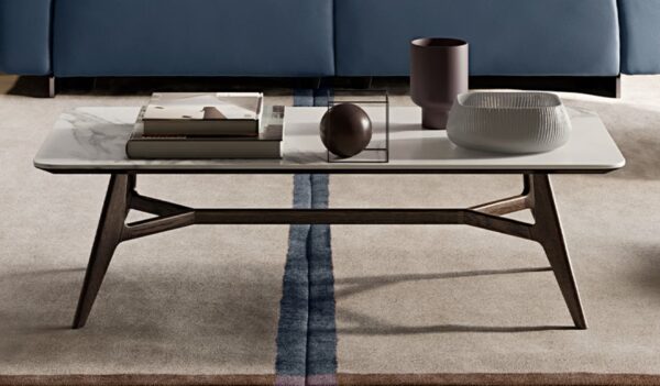 A rectangular marble-top coffee table with wooden legs holds a book, a brown vase, a glass bowl, and a spherical object, set on a beige carpet with a two-tone stripe.