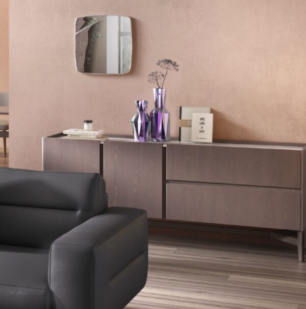 Modern living room featuring a black leather sofa, a wooden sideboard with purple vases, a small mirror, a book, and minimalistic decor. Pale pink walls and hardwood flooring complete the space.
